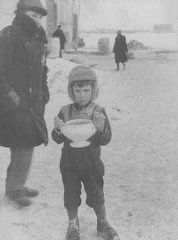 In the Kovno ghetto, a child carries a bowl of soup and holds food ration tickets. Kovno, Lithuania, between 1941 and 1944